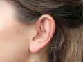 Złoty kolczyk w uchu, ozdobiony cyrkoniami, w trakcie gojenia. Rook piercing wygląda pięknie.
