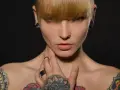 Kobieta z tatuażami na klatce piersiowej i ramionach, kolczykami w uszach i nosie. Czy tatuaże są szkodliwe?