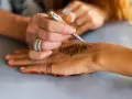 Tworzenie wzoru henny na dłoni, artystka precyzyjnie rysuje tatuaż między palcami, ozdabiając skórę.