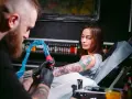 Artysta tworzy świeży tatuaż na ramieniu kobiety. Po sesji będzie musiała unikać pracy fizycznej, by skóra mogła się zagoić.