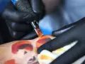 Artysta w czarnych rękawiczkach tworzy kolorowy tatuaż. Pielęgnacja świeżego tatuażu jest kluczowa, a pytanie "ile razy dziennie myc tatuaz" jest ważne dla jego prawidłowego gojenia.