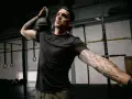 Mężczyzna z małym tatuażem na ramieniu wykonuje ćwiczenie z kettlebell. Intensywny trening w siłowni.