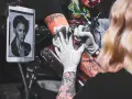 Artysta wykonuje tatuaż twarzy, używając szarego mydła do mycia tatuażu. Na tablecie widnieje wzór.
