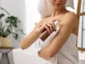 Kobieta aplikuje samoopalacz na ramię, dbając o równomierny koloryt skóry, nawet wokół tatuażu.