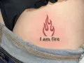 Płomień i napis "I am fire" na skórze, widoczne w okolicach biodra, tuż nad dżinsami. Ten tatuaż na dupie mówi sam za siebie.