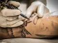 Dłoń w rękawiczce trzyma maszynkę do tatuażu, tworząc wzór na skórze. Po tatuażu może pojawić się osłabienie.