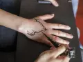 Tworzenie małego tatuażu na dłoni henną. Wzór ozdabia grzbiet dłoni, a artysta precyzyjnie nakłada pastę.