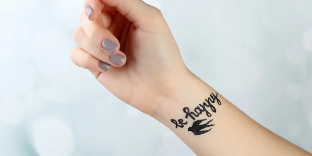 Dłoń z tatuażem "be happy" i ptakiem. Pielęgnacja tatuażu: jak długo smarować, by był piękny.