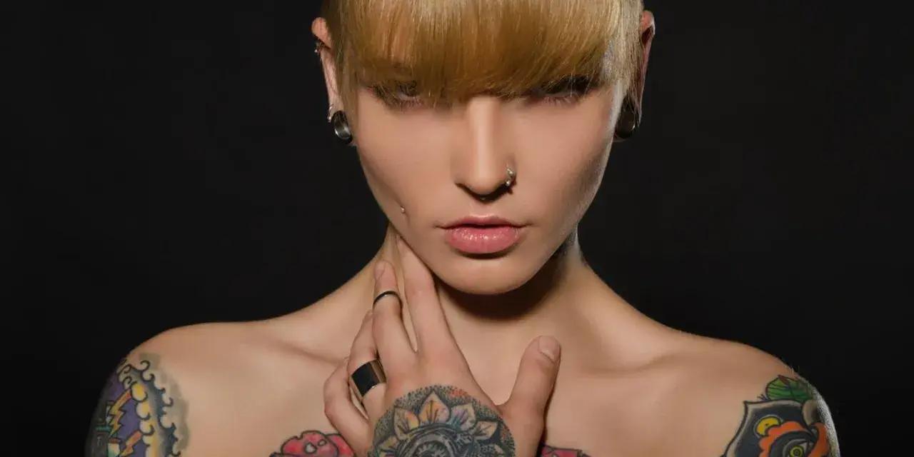 Kobieta z tatuażami na klatce piersiowej i ramionach, kolczykami w uszach i nosie. Czy tatuaże są szkodliwe?