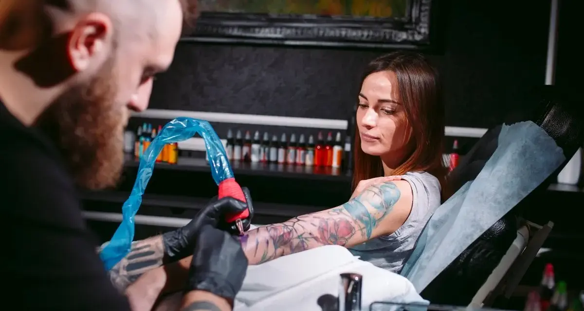 Artysta tworzy świeży tatuaż na ramieniu kobiety. Po sesji będzie musiała unikać pracy fizycznej, by skóra mogła się zagoić.