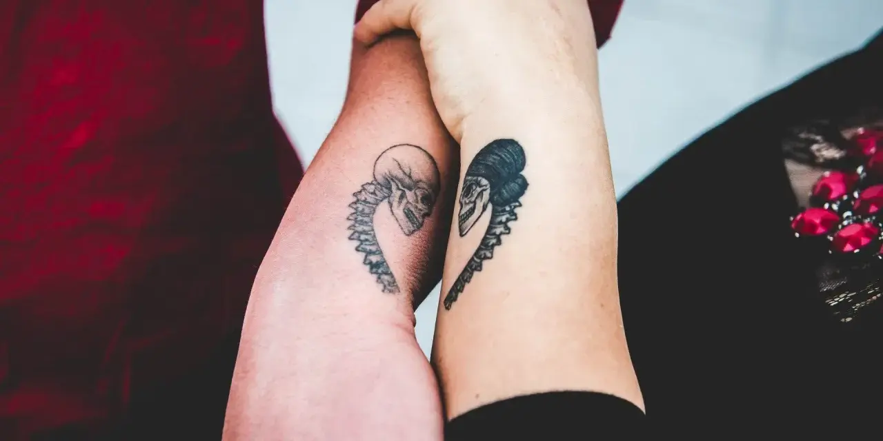 Dwa ramiona z tatuażami czaszek w kształcie serca, symbolizujące tatuaż dla niej i dla niego.