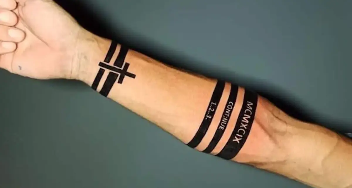 Czarny tatuaż pasek na przedramieniu z krzyżem, napisem "CONTINUE", "1..2..3." i rzymską liczbą MCMXCIX.