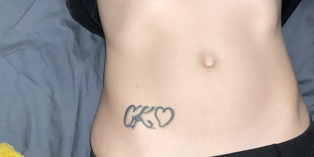 Tatuaz inicjaly CK wplecione w serduszka na brzuchu.