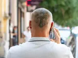 Mężczyzna rozmawia przez telefon, a na jego ogolonej głowie widoczny jest tatuaż krzyża.