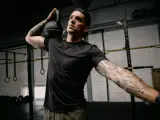 Mężczyzna z małym tatuażem na ramieniu wykonuje ćwiczenie z kettlebell. Intensywny trening w siłowni.
