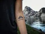 Tatuaż góry na przedramieniu z napisem "ADVENTURE". Symbolizuje miłość do podróży i odkrywania nowych miejsc.