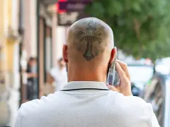 Mężczyzna rozmawia przez telefon, a na jego ogolonej głowie widoczny jest tatuaż krzyża.