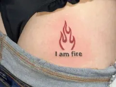 Płomień i napis "I am fire" na skórze, widoczne w okolicach biodra, tuż nad dżinsami. Ten tatuaż na dupie mówi sam za siebie.