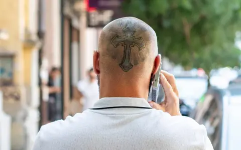 Mężczyzna rozmawia przez telefon, a na jego ogolonej głowie widoczny jest tatuaż krzyża.