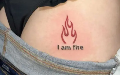 Płomień i napis "I am fire" na skórze, widoczne w okolicach biodra, tuż nad dżinsami. Ten tatuaż na dupie mówi sam za siebie.