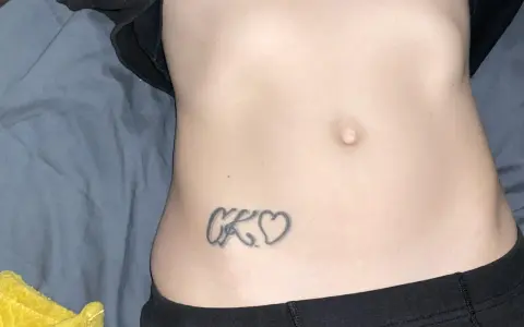 Tatuaz inicjaly CK wplecione w serduszka na brzuchu.