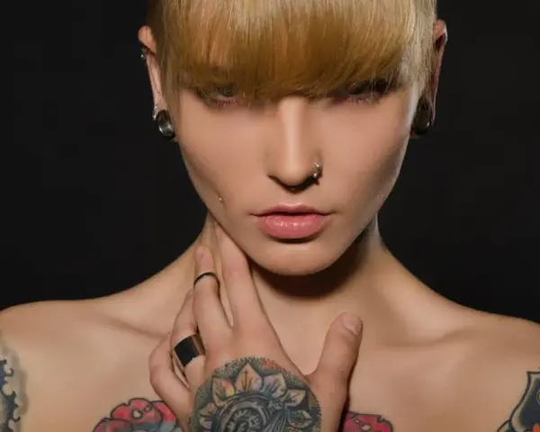 Kobieta z tatuażami na klatce piersiowej i ramionach, kolczykami w uszach i nosie. Czy tatuaże są szkodliwe?