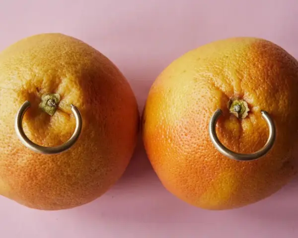 Dwa grejpfruty z kółkami imitującymi, ile goi się kolczyk w sutku.