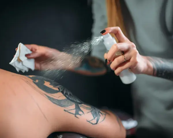 Artysta spryskuje skórę klienta, przygotowując ją do dalszej pracy. Dobre pytanie, jakie mydło do tatuażu wybrać, by zapewnić najlepsze efekty i higienę.