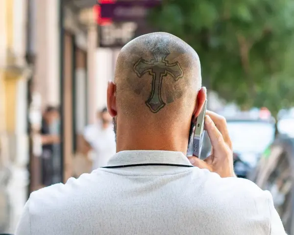 Mężczyzna rozmawia przez telefon, a na jego ogolonej głowie widoczny jest tatuaż krzyża.