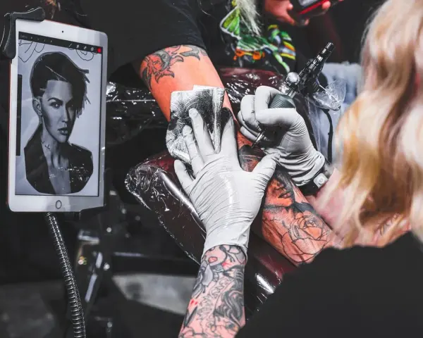 Artysta wykonuje tatuaż twarzy, używając szarego mydła do mycia tatuażu. Na tablecie widnieje wzór.