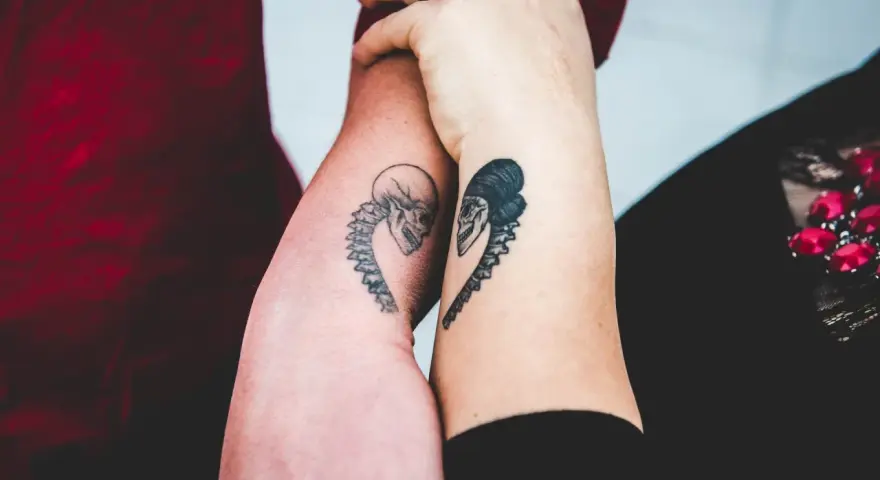 Dwa ramiona z tatuażami czaszek w kształcie serca, symbolizujące tatuaż dla niej i dla niego.